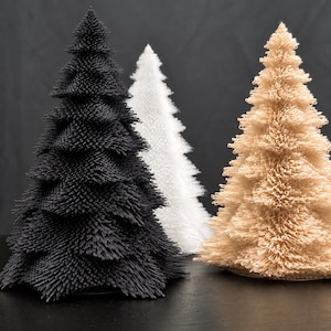 May include: Three conical tree-shaped sculptures with a textured, needle-like surface. One tree is black, one is white, and one is a light tan colour. Each sculpture features a dense, layered structure that mimics the appearance of pine needles.