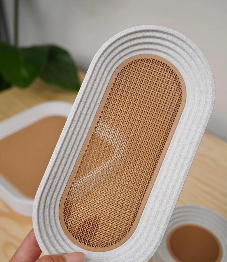 May include: An oval-shaped tray with a textured, light gray border and a tan mesh center. The tray has a ribbed design around the edge. Another tray is visible in the background.