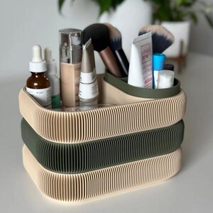 May include: A three-tiered organizer for cosmetics and beauty products. The top and bottom tiers are beige, and the middle tier is olive green. The organizer is filled with makeup brushes, skincare products, and tubes of creams.
