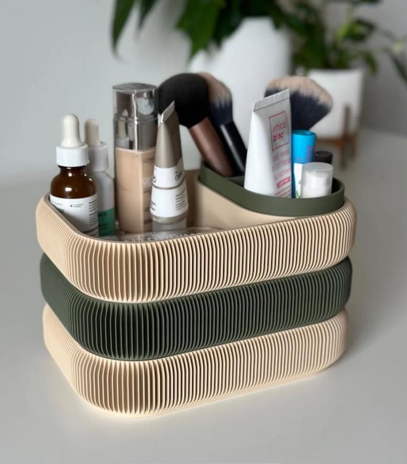 May include: A three-tiered organizer for cosmetics and beauty products. The top and bottom tiers are beige, and the middle tier is olive green. The organizer is filled with makeup brushes, skincare products, and tubes of creams.