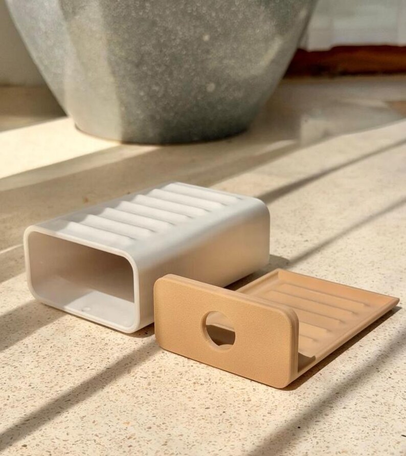 May include: A white rectangular soap dish with a ribbed surface and a hollow interior, accompanied by a separate tan-colored insert featuring a circular cutout and a matching ribbed design, both constructed from a smooth, solid material.