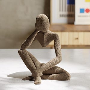 May include: A textured, beige sculpture of a person in a seated, thinking pose. The figure has a minimalist design, with the head resting on the hand. The sculpture is approximately 25 cm tall and is suitable for home decor.