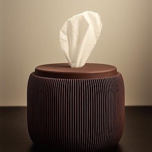 May include: A brown tissue box with a cylindrical shape and vertical ribbed design. A white tissue is pulled from the top. The tissue box is made of a dark brown material and sits on a dark surface.