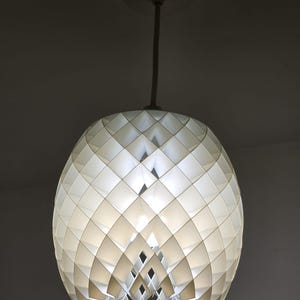May include: A white, geometric pendant light fixture. The light has a spherical shape, constructed from diamond-shaped panels. The fixture hangs from a white cord and ceiling mount, creating a modern, decorative lighting element.