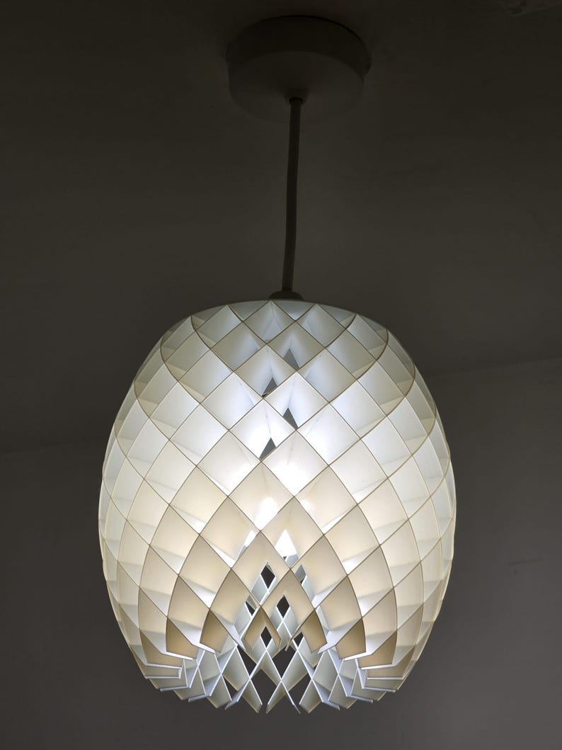 May include: A white, geometric pendant light fixture. The light has a spherical shape, constructed from diamond-shaped panels. The fixture hangs from a white cord and ceiling mount, creating a modern, decorative lighting element.