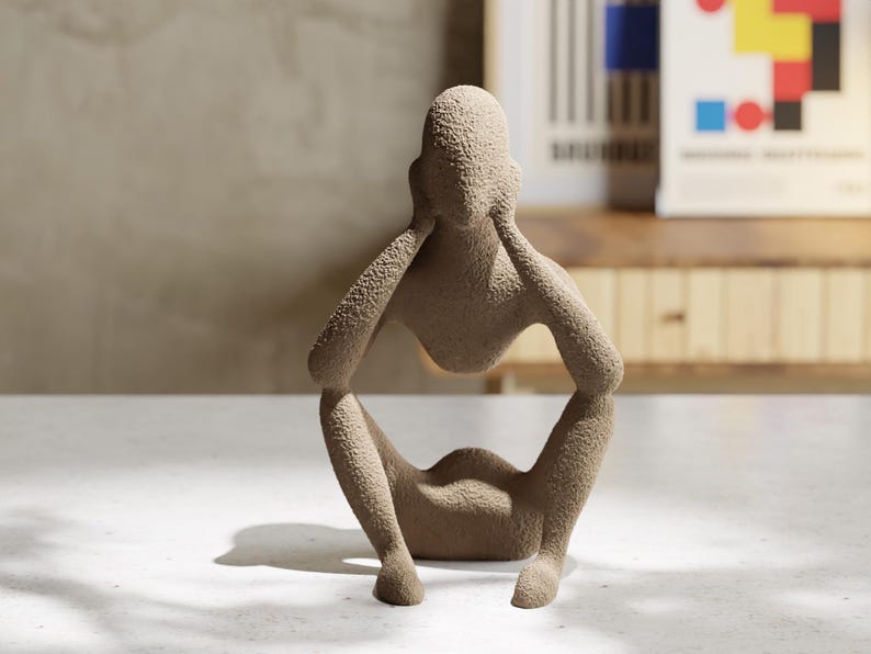 May include: A beige, textured sculpture of a seated figure with arms raised to the head. The figure has a rough, granular surface finish and a hollow torso area. The form is abstract, depicting a person in a crouched position with knees bent.