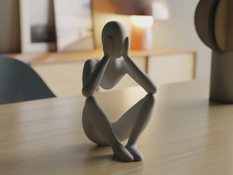 May include: A matte light gray sculpture of a seated human figure with a textured surface. The figure is depicted in a hunched position with both hands raised to cover the face, elbows resting on the knees, creating a contemplative posture.