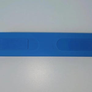 May include: A long, horizontal, blue plastic case with rounded ends. The top surface features two recessed, elongated oval sections positioned symmetrically along the center, providing a smooth, uniform appearance for this storage container.