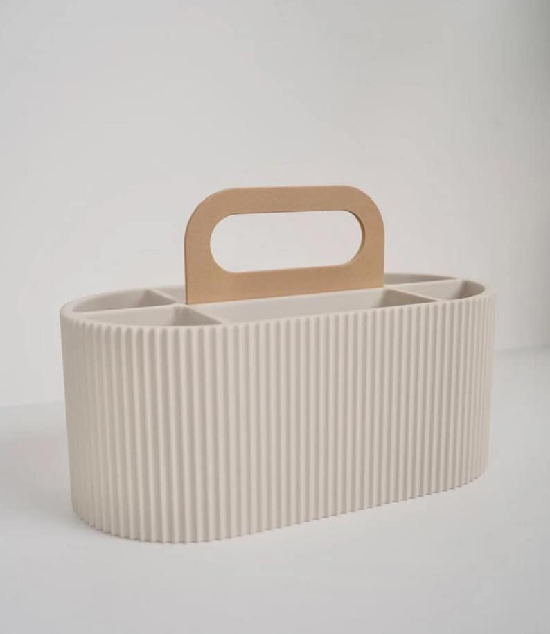May include: A beige, ribbed, oval-shaped organizer with a light brown handle. The organizer has multiple compartments inside. The handle is a light brown color and is attached to the top of the organizer.