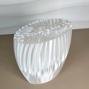 May include: A translucent, oval-shaped decorative bowl with a textured, ridged exterior. The bowl's design features vertical, wave-like patterns that create a sense of depth and light reflection. The interior has a unique, organic texture.