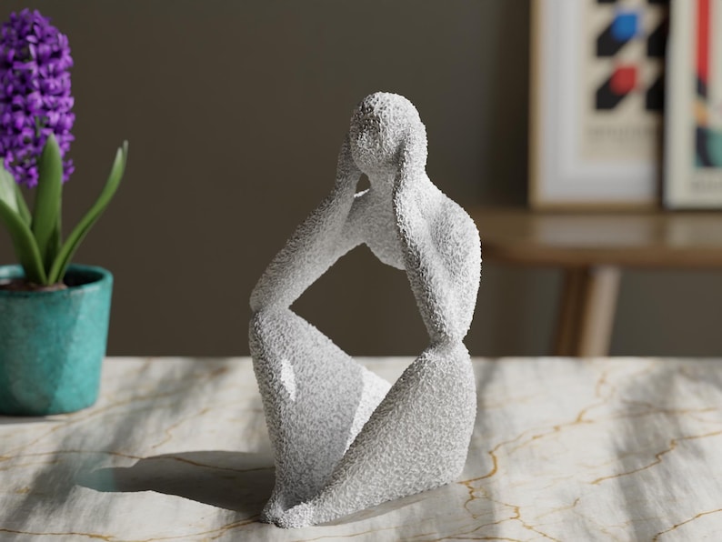 May include: A white abstract sculpture of a seated figure with a textured, granular surface. The figure is depicted in a contemplative pose with both hands raised to the sides of the head. The sculpture has a smooth, curved silhouette.