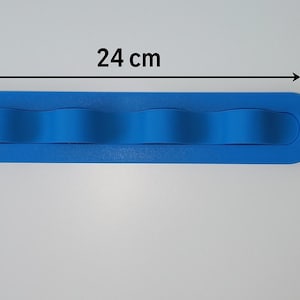 May include: A bright blue, elongated, oval-shaped silicone organizer with four rounded, wave-like dividers. The object measures 24 cm in length and 5 cm in width, as indicated by the black text and arrows printed directly on the image.