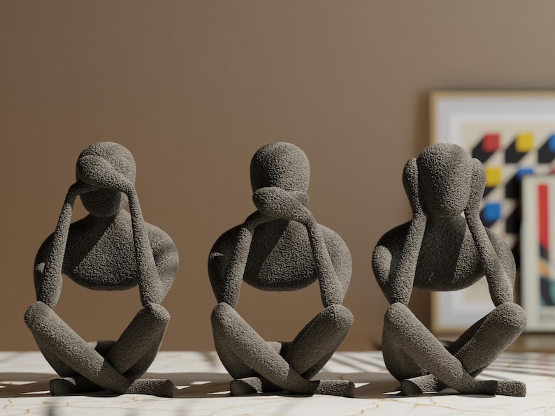 K&ouml;nnte beinhalten: Drei graue Skulpturen in sitzender Pose, jede mit H&auml;nden, die Augen, Ohren und Mund bedecken. Die Figuren haben eine strukturierte Oberfl&auml;che und sind auf einer gemusterten Oberfl&auml;che angeordnet. Der Hintergrund ist neutral gef&auml;rbt.