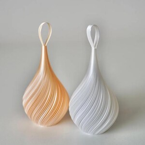 May include: Two teardrop-shaped ornaments with a spiraling, layered texture. One ornament is a soft peach color, and the other is a crisp white. Each piece features a matching ribbon loop at the top for hanging, creating a symmetrical display.