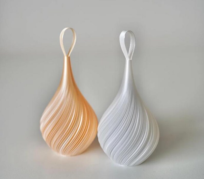 May include: Two teardrop-shaped ornaments with a spiraling, layered texture. One ornament is a soft peach color, and the other is a crisp white. Each piece features a matching ribbon loop at the top for hanging, creating a symmetrical display.