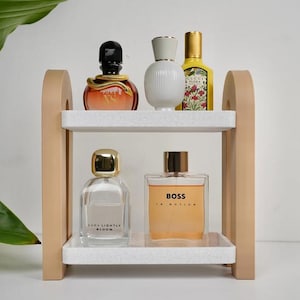 May include: A two-tiered wooden shelf with white speckled shelves displays various perfume bottles. The bottles vary in shape, size, and color, including a bottle with a snake design, a white ribbed bottle, and a yellow bottle.