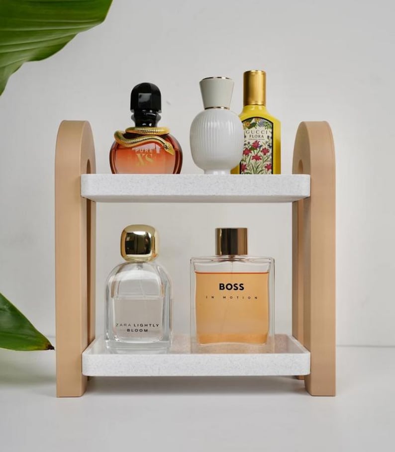 May include: A two-tiered wooden shelf with white speckled shelves displays various perfume bottles. The bottles vary in shape, size, and color, including a bottle with a snake design, a white ribbed bottle, and a yellow bottle.