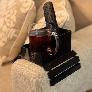 Puede incluir: Una bandeja negra para el brazo del sof&aacute; con un portavasos incorporado y almacenamiento para el mando a distancia. Una taza de vidrio transparente llena de t&eacute; se encuentra en el portavasos. La bandeja est&aacute; dise&ntilde;ada para descansar sobre el brazo de un sof&aacute;.