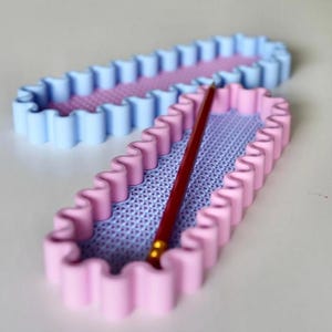 May include: Two rectangular pencil holders with wavy edges. One is light blue, the other is pink. Both have a textured lavender interior. A red pencil rests inside the pink holder. These are ideal for desk organization.