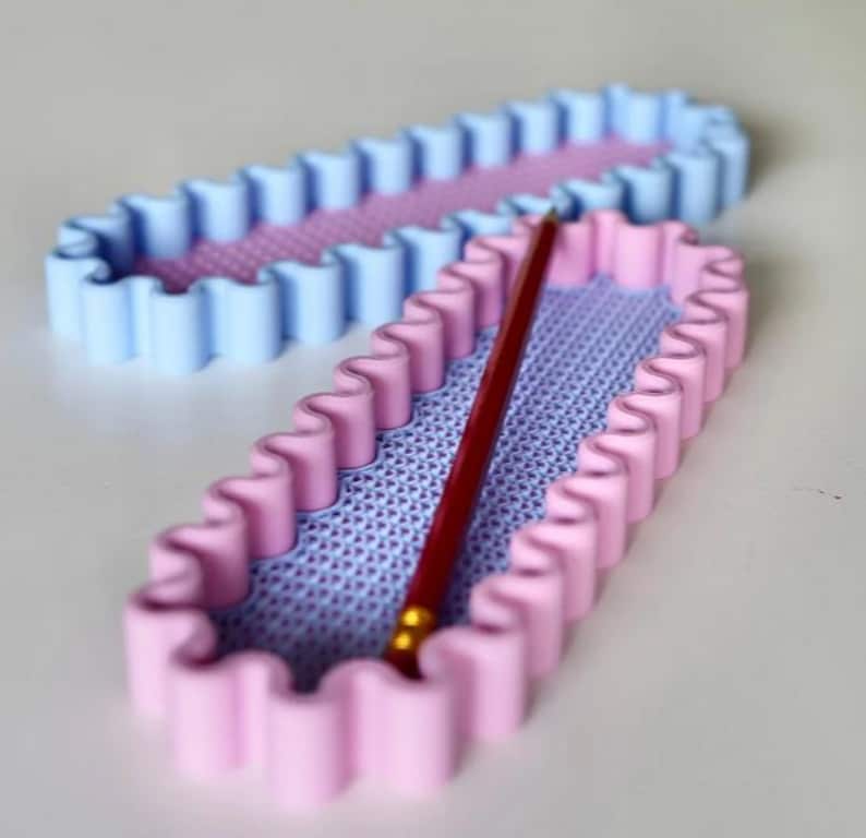 May include: Two rectangular pencil holders with wavy edges. One is light blue, the other is pink. Both have a textured lavender interior. A red pencil rests inside the pink holder. These are ideal for desk organization.