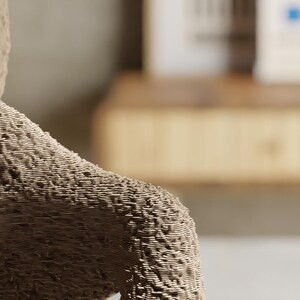 May include: Close-up of a textured, beige sculpture of a teddy bear's arm and shoulder. The bear's fur appears to be made of layered lines, creating a unique, tactile surface. The background is blurred.