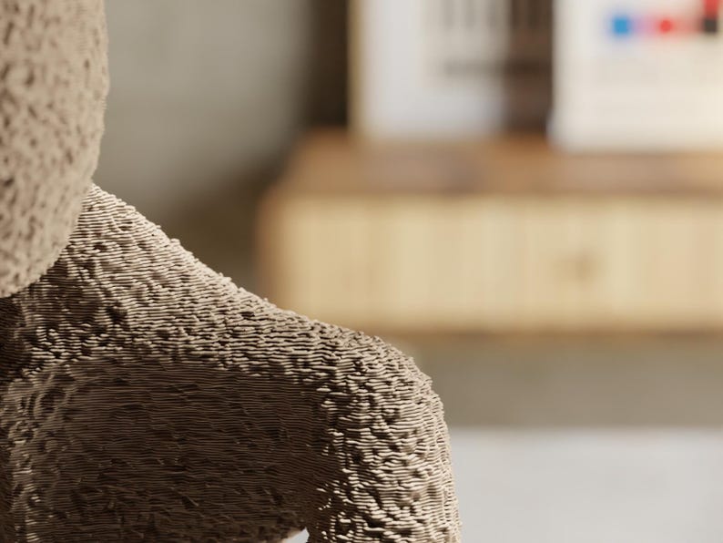 May include: Close-up of a textured, beige sculpture of a teddy bear's arm and shoulder. The bear's fur appears to be made of layered lines, creating a unique, tactile surface. The background is blurred.