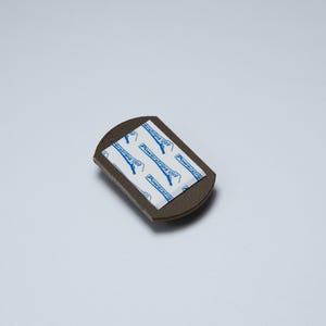 May include: A small, dark brown, semi-circular adhesive mounting piece with a flat top edge. The centre features a white rectangular adhesive pad with blue text that reads Powerstrips and includes a small icon of a hand pulling a tab.