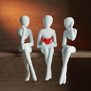 May include: Three white abstract figurines sit on a wooden shelf. The central figure holds a red heart. The other two figures are in pensive poses, one with a hand on their chin, the other with a hand on their head. The background is a warm, neutral tone.