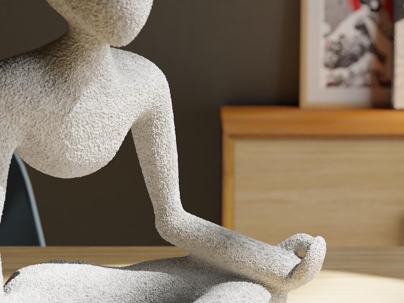 May include: A textured, white sculpture of a person in a seated yoga pose. The figure's arms are extended, with the hands resting in a meditative position. The sculpture is on a wooden surface, with a blurred background.