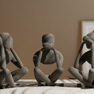 K&ouml;nnte beinhalten: Drei graue abstrakte Skulpturen in sitzender Pose, jede mit H&auml;nden, die Augen, Ohren und Mund bedecken. Die Figuren haben eine strukturierte Oberfl&auml;che und sind auf einer marmor&auml;hnlichen Oberfl&auml;che angeordnet. Ein gerahmtes Kunstwerk befindet sich im Hintergrund.