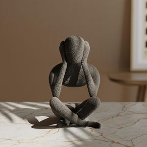 K&ouml;nnte beinhalten: Graue Skulptur einer sitzenden Person, die sich die Ohren zuh&auml;lt. Die Figur hat eine strukturierte Oberfl&auml;che und befindet sich auf einer marmorierten Oberfl&auml;che. Die Skulptur ist ein dekoratives Objekt.