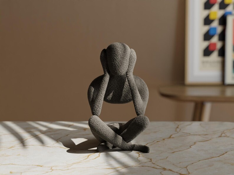 K&ouml;nnte beinhalten: Graue Skulptur einer sitzenden Person, die sich die Ohren zuh&auml;lt. Die Figur hat eine strukturierte Oberfl&auml;che und befindet sich auf einer marmorierten Oberfl&auml;che. Die Skulptur ist ein dekoratives Objekt.