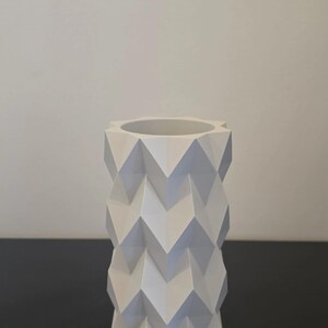 Puede incluir: Un jarr&oacute;n blanco geom&eacute;trico con un patr&oacute;n en zigzag. El jarr&oacute;n es cil&iacute;ndrico con una amplia abertura en la parte superior. El dise&ntilde;o es moderno y minimalista, adecuado para la decoraci&oacute;n del hogar.