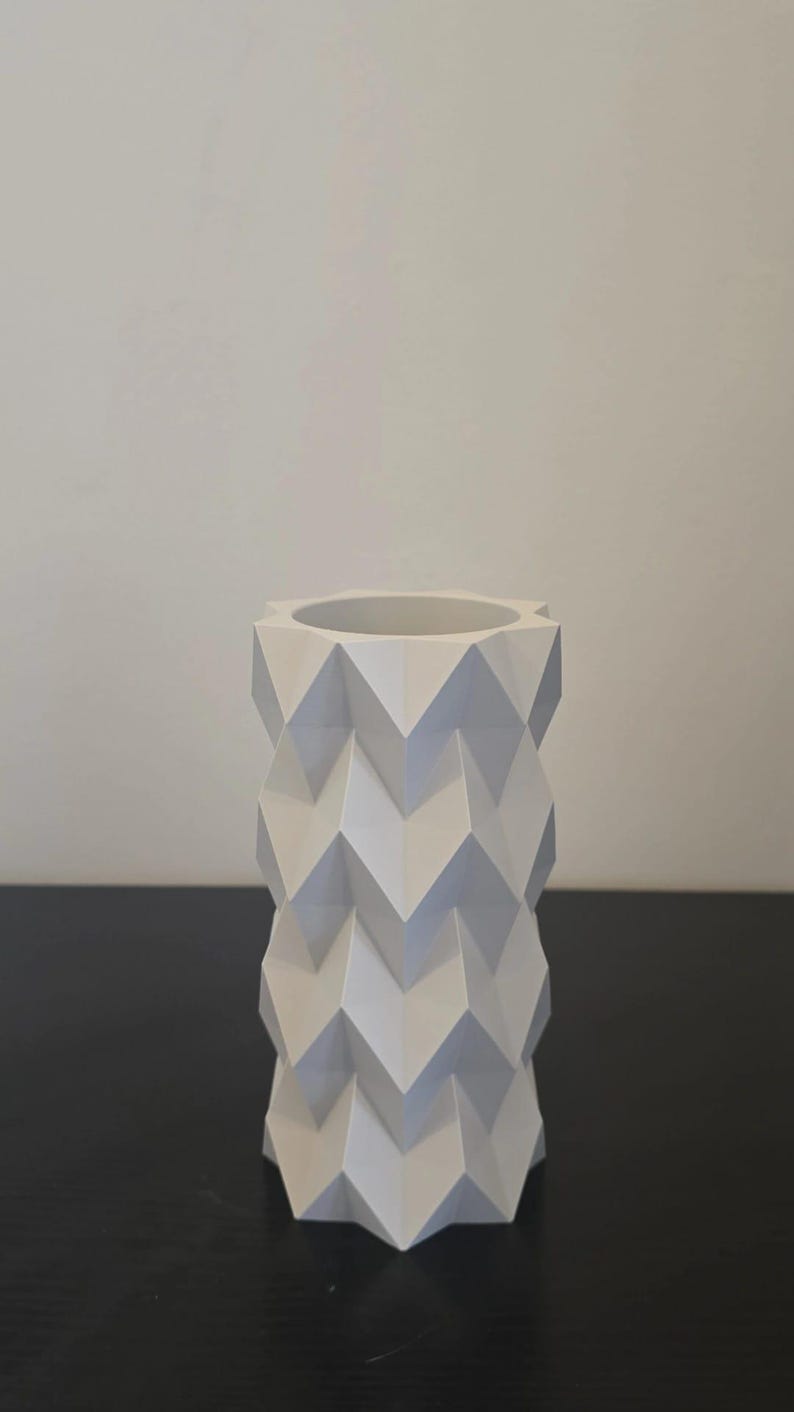 Puede incluir: Un jarr&oacute;n blanco geom&eacute;trico con un patr&oacute;n en zigzag. El jarr&oacute;n es cil&iacute;ndrico con una amplia abertura en la parte superior. El dise&ntilde;o es moderno y minimalista, adecuado para la decoraci&oacute;n del hogar.