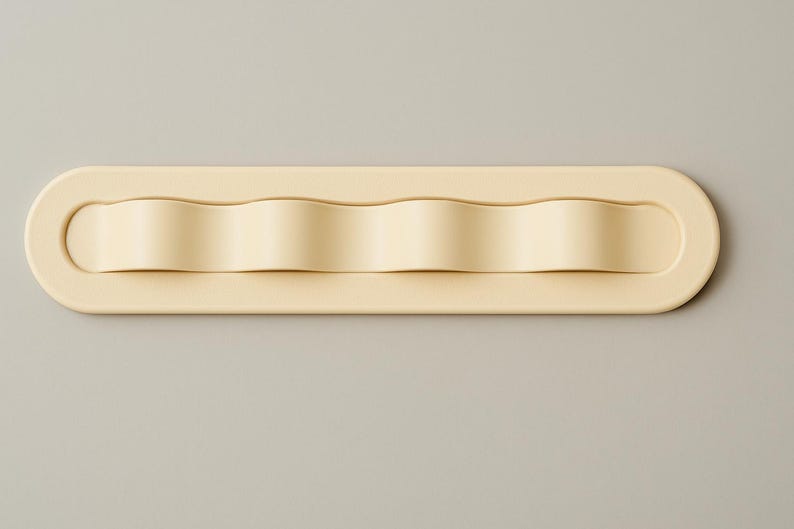 May include: A cream-colored, elongated, rectangular wall hook with rounded ends. The central section features four distinct, wave-like protrusions that create a series of curved, recessed spaces along the length of the object.