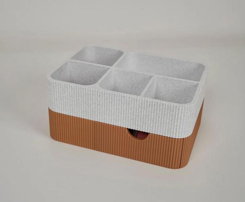 May include: A two-tone organizer with a textured, ribbed design. The top section is white with multiple compartments, while the bottom is brown with a small drawer. Ideal for storing small items.