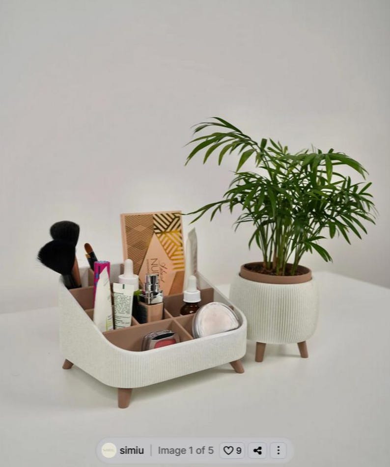 Puede incluir: Un organizador de maquillaje blanco y marr&oacute;n con varios productos de belleza y brochas. Una planta en maceta con hojas verdes est&aacute; a la derecha. El organizador tiene varios compartimentos y est&aacute; sobre patas de madera.