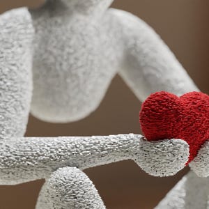 Puede incluir: Escultura blanca de una figura sosteniendo un coraz&oacute;n rojo. La figura est&aacute; texturizada con peque&ntilde;as piezas individuales, d&aacute;ndole una apariencia &uacute;nica, casi pixelada. El coraz&oacute;n es de un rojo vibrante, contrastando con la figura blanca.