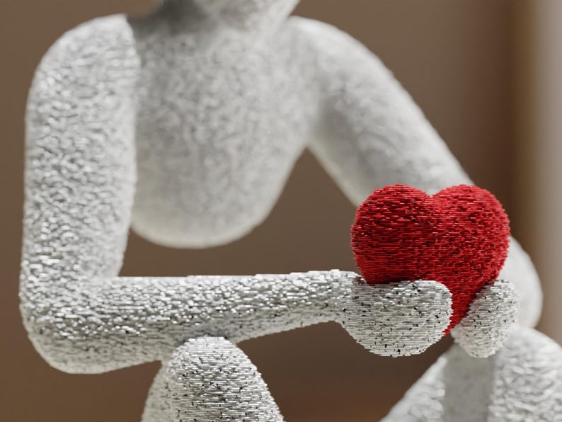 Puede incluir: Escultura blanca de una figura sosteniendo un coraz&oacute;n rojo. La figura est&aacute; texturizada con peque&ntilde;as piezas individuales, d&aacute;ndole una apariencia &uacute;nica, casi pixelada. El coraz&oacute;n es de un rojo vibrante, contrastando con la figura blanca.