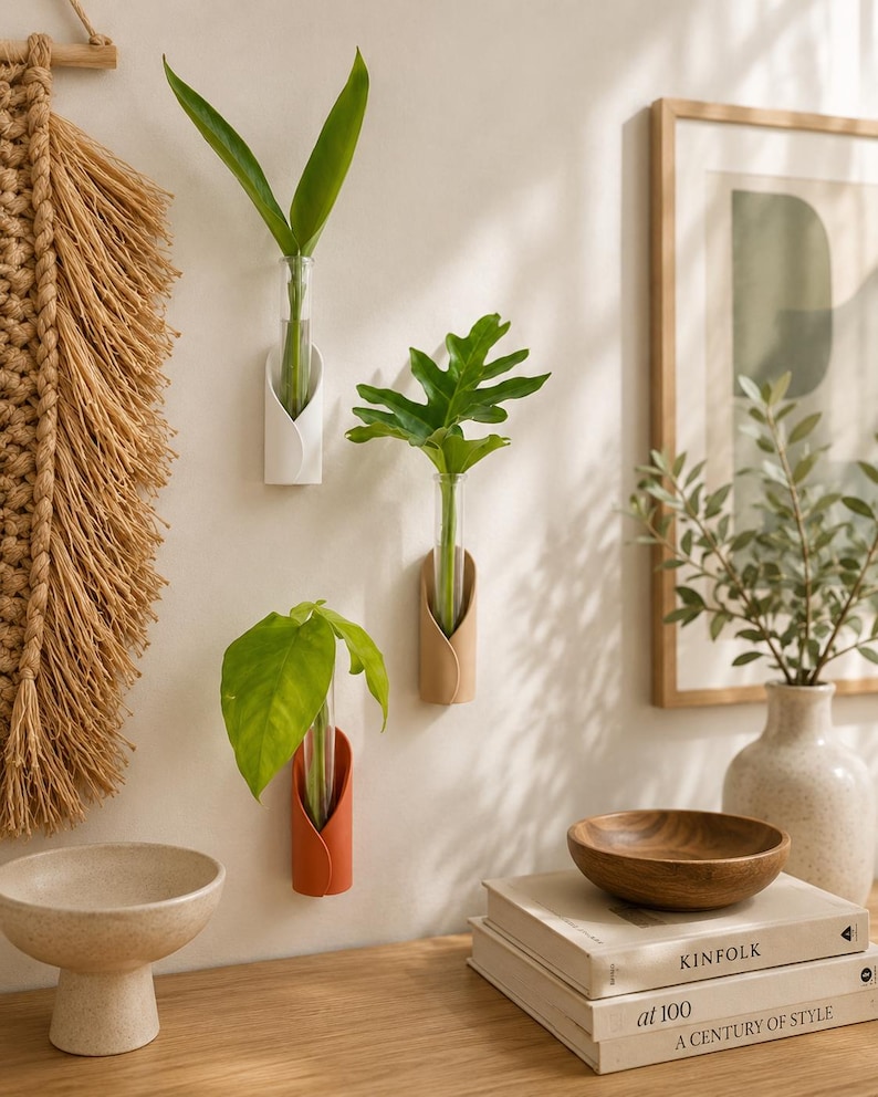 May include: Three wall-mounted plant propagation stations, each featuring a clear glass test tube held by a curved, petal-shaped holder in white, beige, and terracotta colours, with green leaves placed inside each glass tube for display.