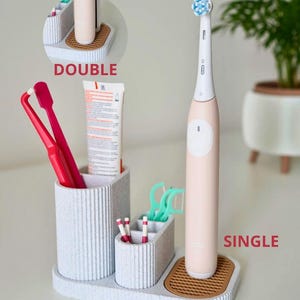 May include: A light gray toothbrush holder with multiple compartments. The holder has a textured, ribbed design and includes a section for an electric toothbrush, toothpaste, floss, and toothbrushes. The word "SINGLE" is visible.