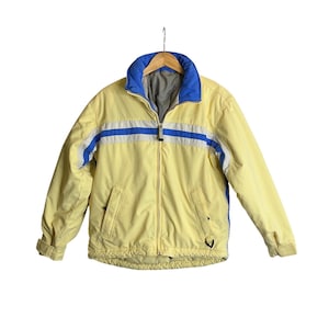 May include: A yellow jacket with blue and white stripes across the chest. The jacket has a blue collar and a full zipper. It is hanging on a wooden hanger against a white background.