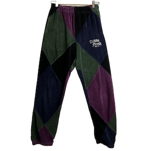 Puede incluir: Pantalones deportivos multicolores con un patrón de diamantes en tonos verdes, morados, negros y azul marino. El texto "Teddy Fresh" está bordado en la pierna derecha. Los pantalones están hechos de un material suave y aterciopelado.