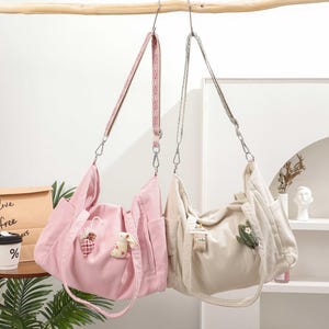 May include: Two corduroy shoulder bags suspended from a wooden rod. One is pale pink with a heart and bunny charm, the other is cream-coloured with a cactus patch. Both have adjustable straps and silver hardware.