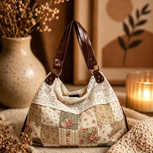 Könnte beinhalten: Eine Handtasche im Hobo-Stil mit einem Patchwork-Stoffkörper, der verschiedene florale Muster in Grün-, Rosa- und Cremetönen aufweist. Der obere Bereich ist mit weißer Spitzenborte verziert und die Tasche hat zwei braune Kunstledergriffe mit Goldringen.