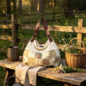 May include: A hobo-style handbag featuring a patchwork fabric body with a floral pattern in shades of green, pink, and cream. The bag has a wide white lace trim along the top edge and two dark brown leather handles attached with metal rings.
