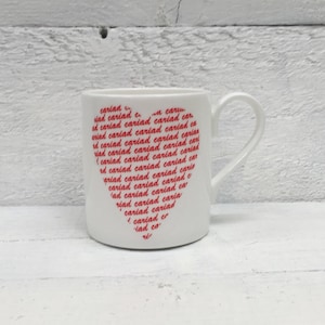 May include: White ceramic mug with a red heart design. The heart is made up of the word "cariad" repeated many times.