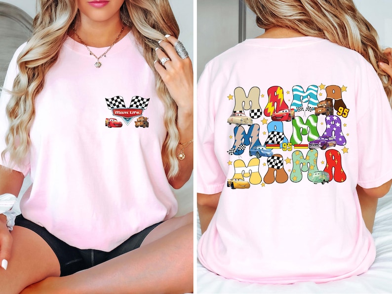 May include: Light pink t-shirt featuring a front pocket design with checkered flags and cartoon cars. The back of the shirt displays the word "MAMA" in a colorful, playful font, with car illustrations and the number "95".