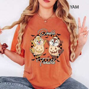 May include: Orange t-shirt with a Halloween graphic. The design shows two cartoon chipmunks dressed as pumpkins, with the words "Double Trouble". Bats are around the chipmunks. The t-shirt is a comfortable fit.