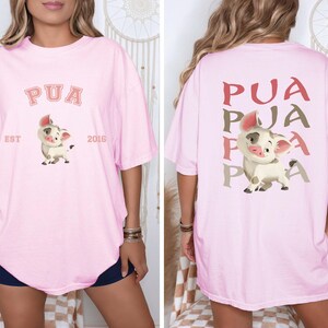 May include: Pale pink oversized t-shirt with a cartoon pig design. The front displays "PUA" above the pig, with "EST 2016" below. The back of the shirt has "PUA" repeated three times in a vertical pattern.
